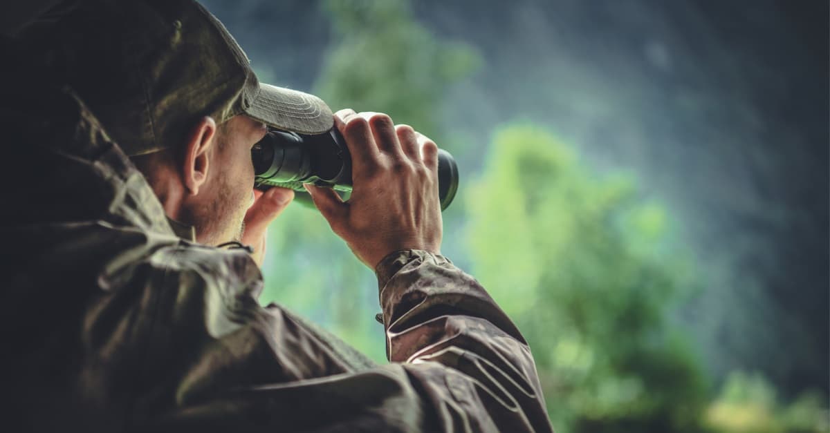 caucasian hunter in masking camouflage uniform with binoculars